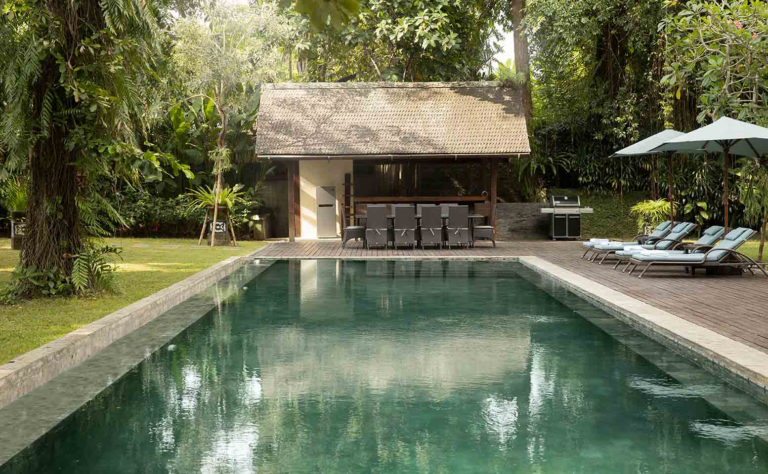 Villa Tirtadari - pool with lounge chairs and umbrellas in the middle of a lush tropical garden.